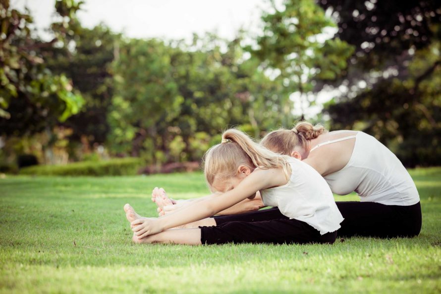 Mother and daughter doing yoga exercises on grass in the park.